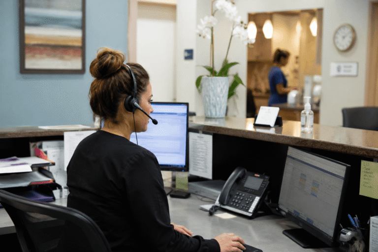 Front desk staff member at a medical practice using a headset while managing phone, text, voicemail, and video communication.